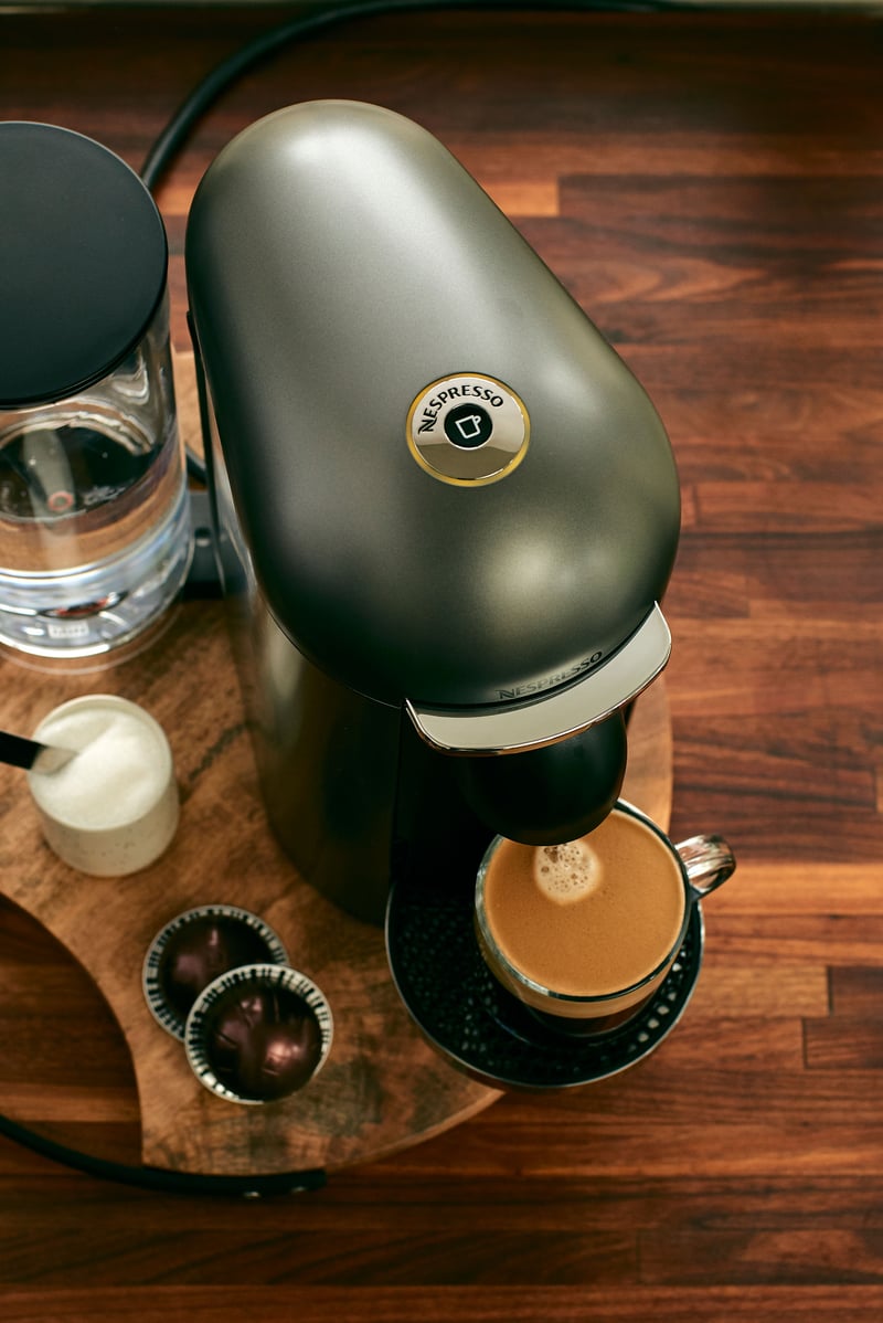 A dark green Nespresso machine on a wooden counter with a filled cup and capsules