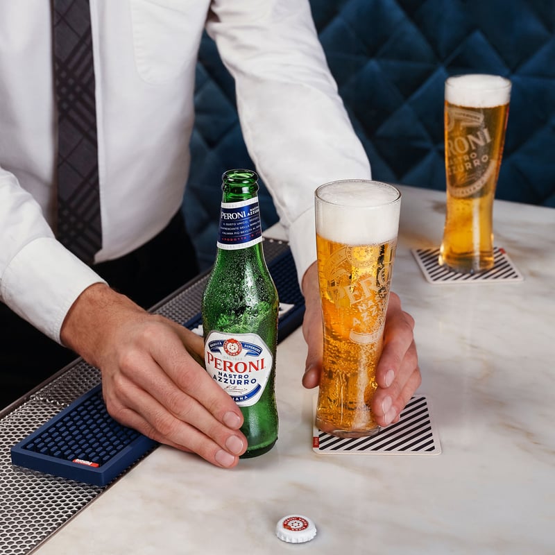 A bartender sets down a poured lager beside its bottle on a marble bar