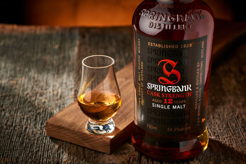 A Springbank 15 bottle beside a Glencairn glass of whisky on a wooden board