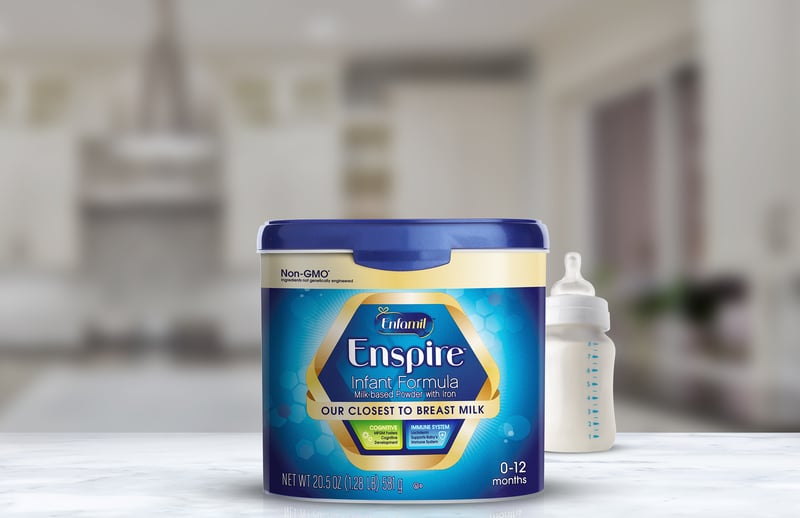 A tub of Enspire infant formula with bottles beside it in a soft-focus kitchen