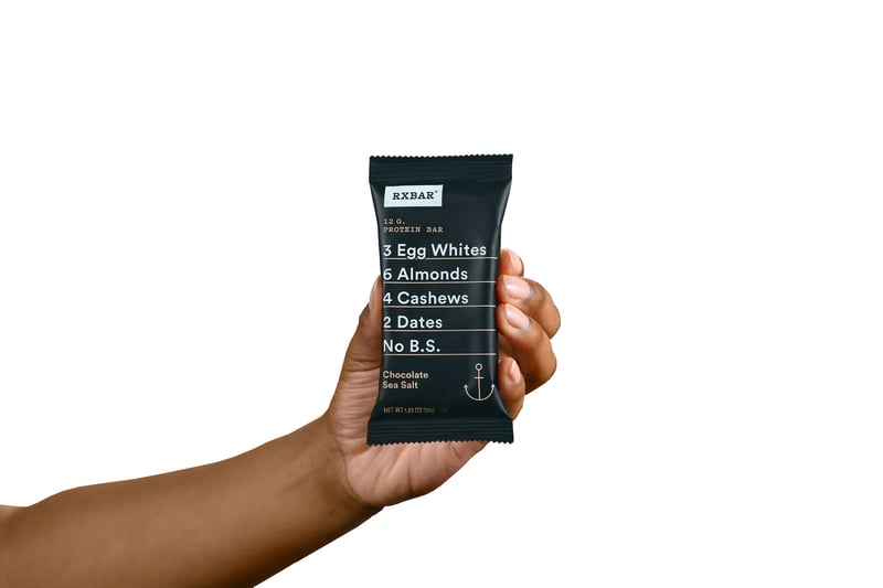 A hand holds up a wrapped RXBAR protein bar against white
