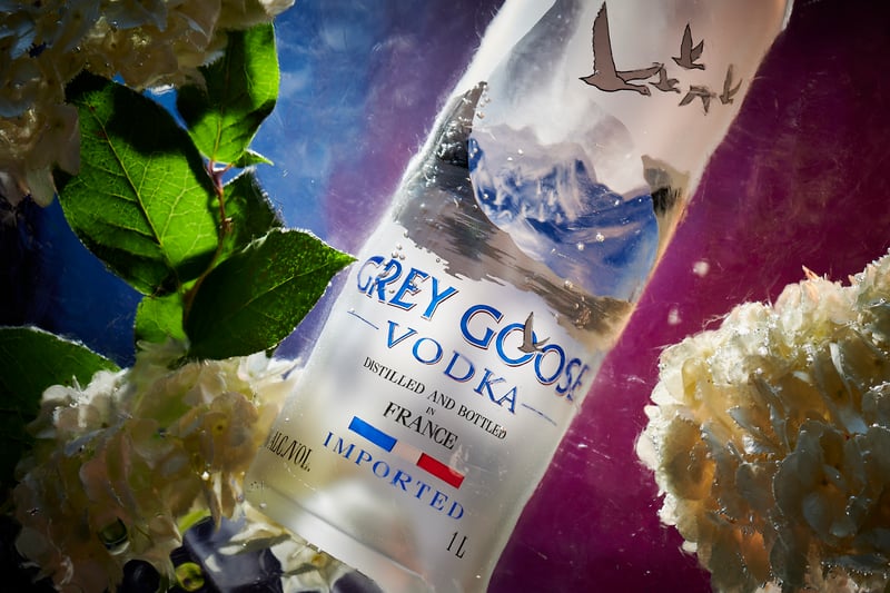 A Grey Goose vodka bottle lying among mint leaves and pale flowers under cool light