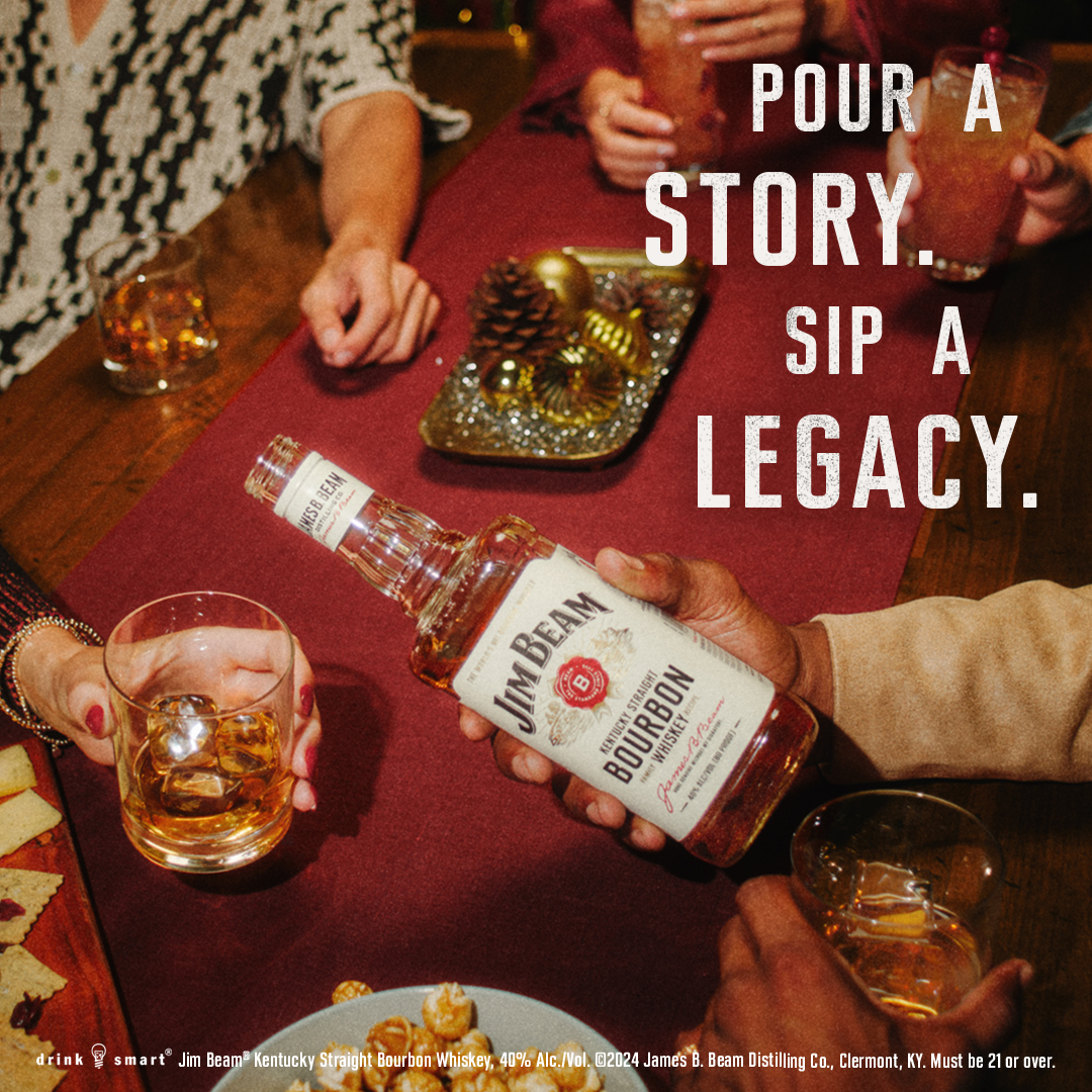 Hands lift bourbon glasses from a red table beside a Jim Beam bottle under the line Pour a story, sip a legacy
