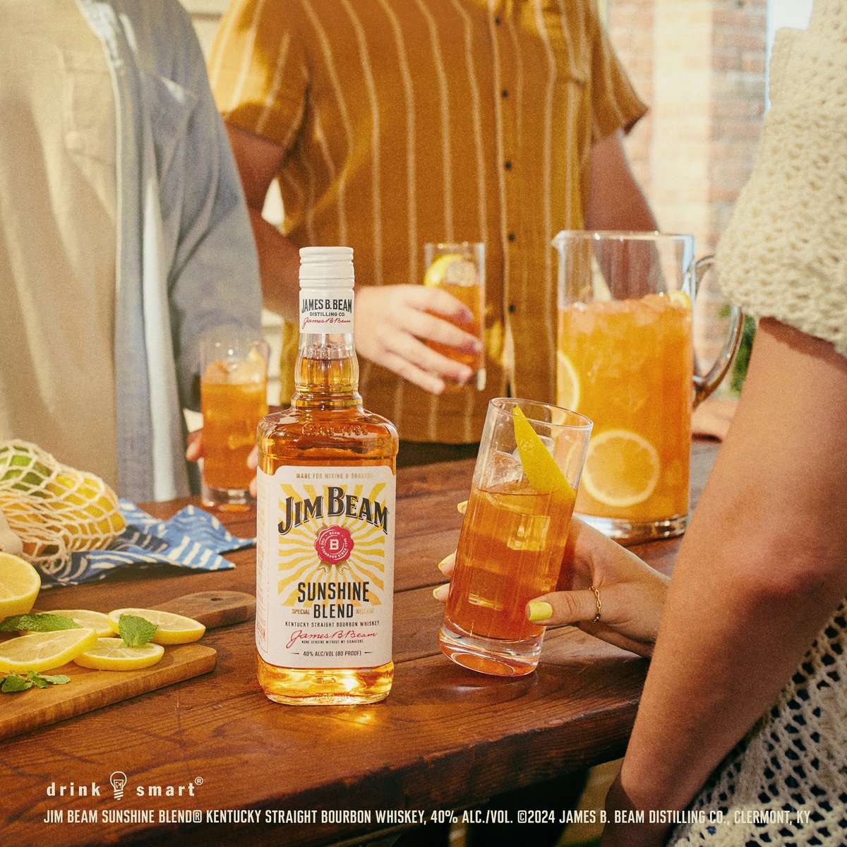 People reach for tall iced bourbon highballs garnished with citrus on a wooden table