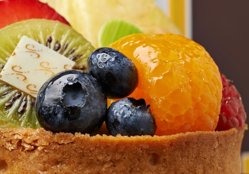 A close crop of a fruit tart topped with blueberries, kiwi and apricot glaze