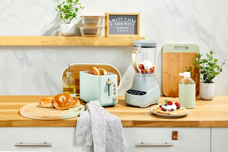 A kitchen counter styled with a mint toaster, blender and kettle beside pastries and a chopping board