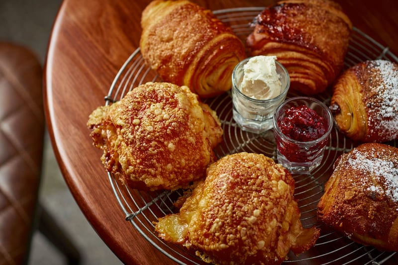 A wire basket of croissants and crumb-topped pastries with small jars of jam and cream