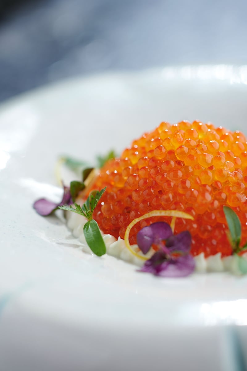 A spoonful of salmon roe with edible flowers plated on white