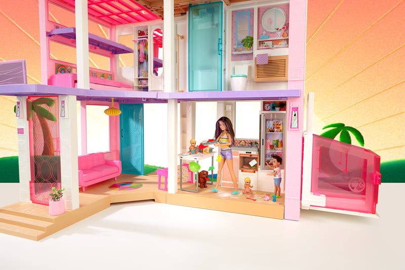 A pink Barbie dreamhouse playset shown open across three floors with dolls and furniture