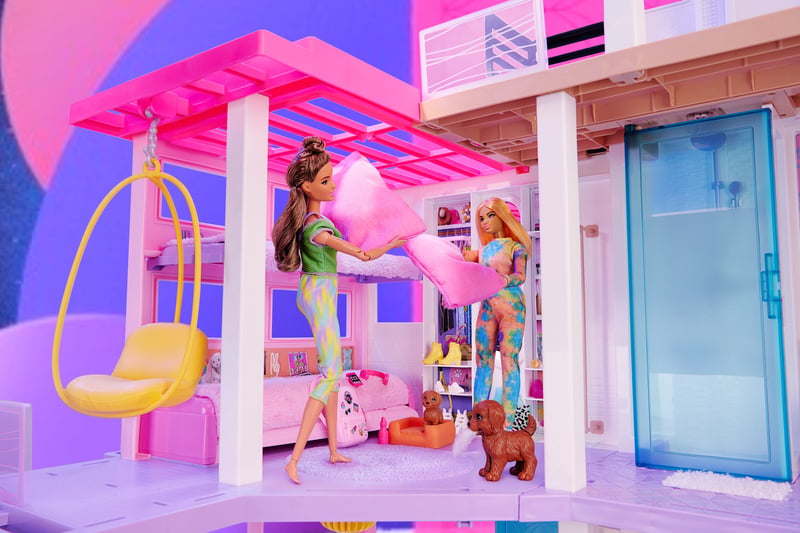 A pink Barbie dreamhouse playset with dolls, a hanging egg chair and a slide in saturated color