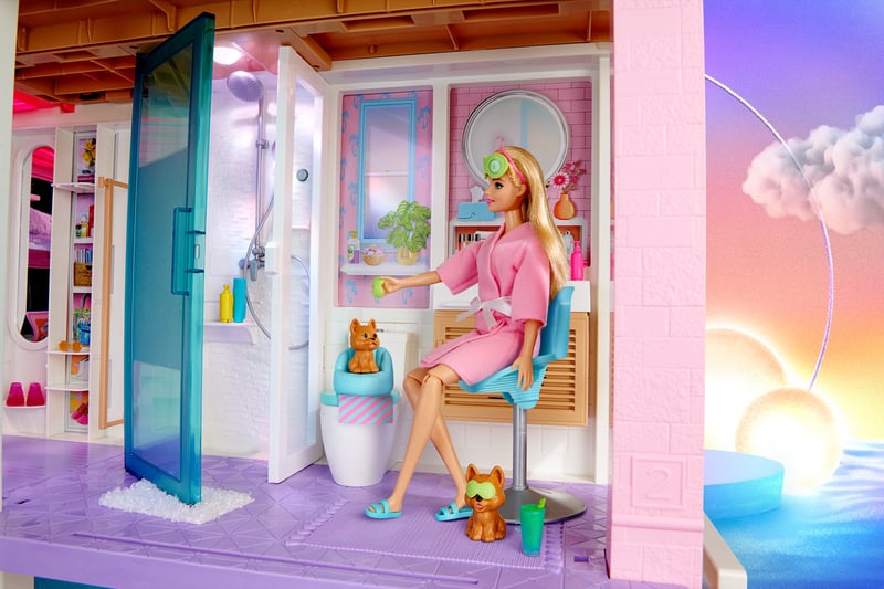 A Barbie doll seated in a pastel playset bathroom with a bathtub and a small dog