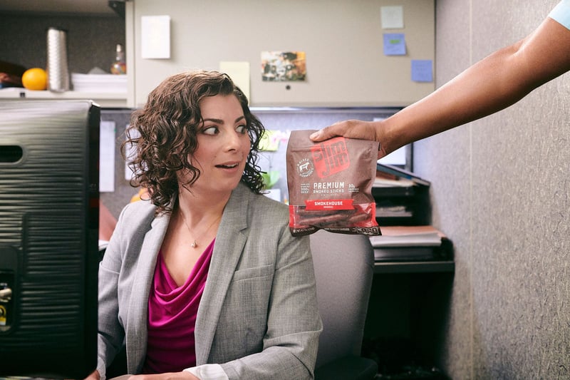 A woman at an office desk turns as a colleague hands her a package of frozen food