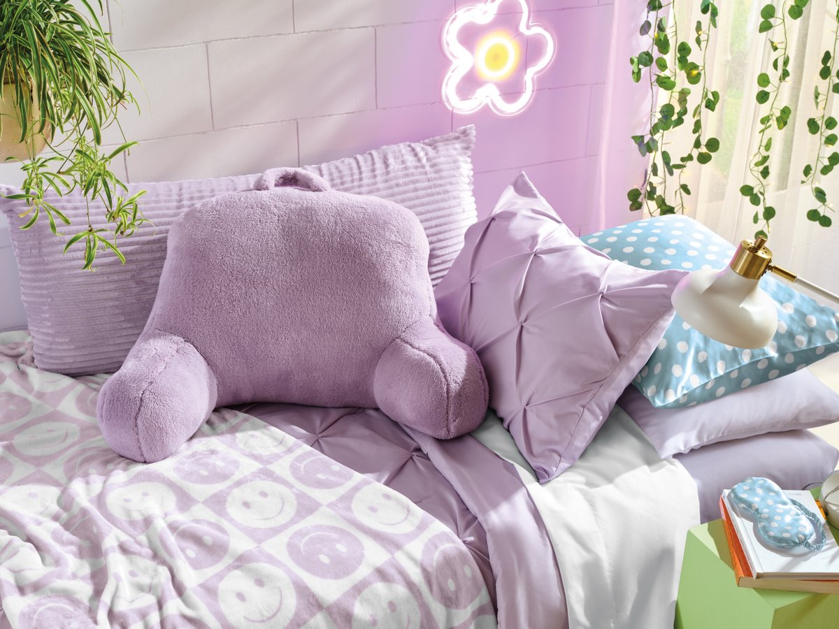 A lilac bedroom with fluffy cushions, a flower wall decal and plants above the bed