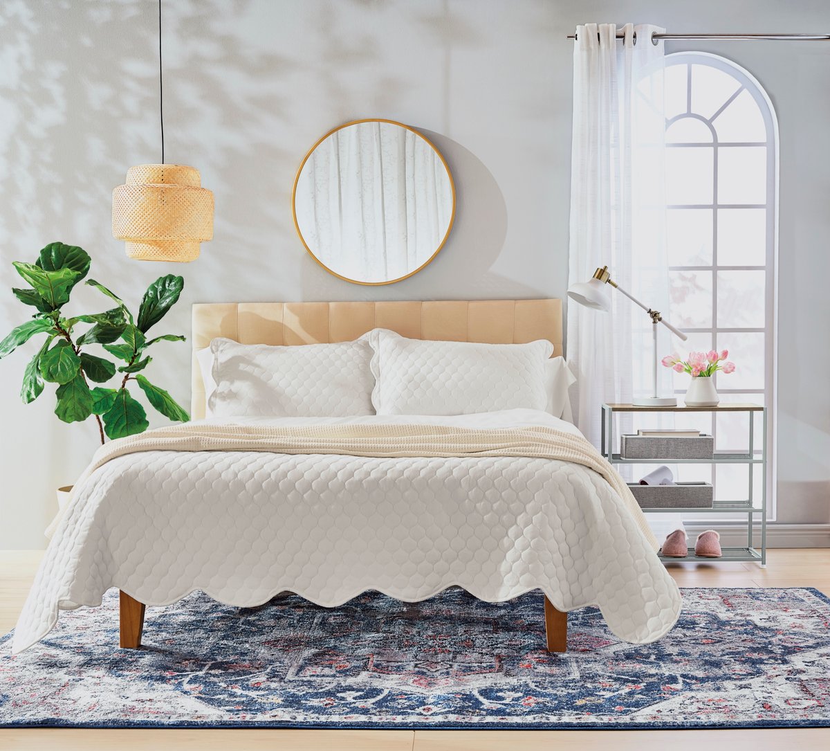 A cream bedroom with a round mirror, arched window and a woven pendant light