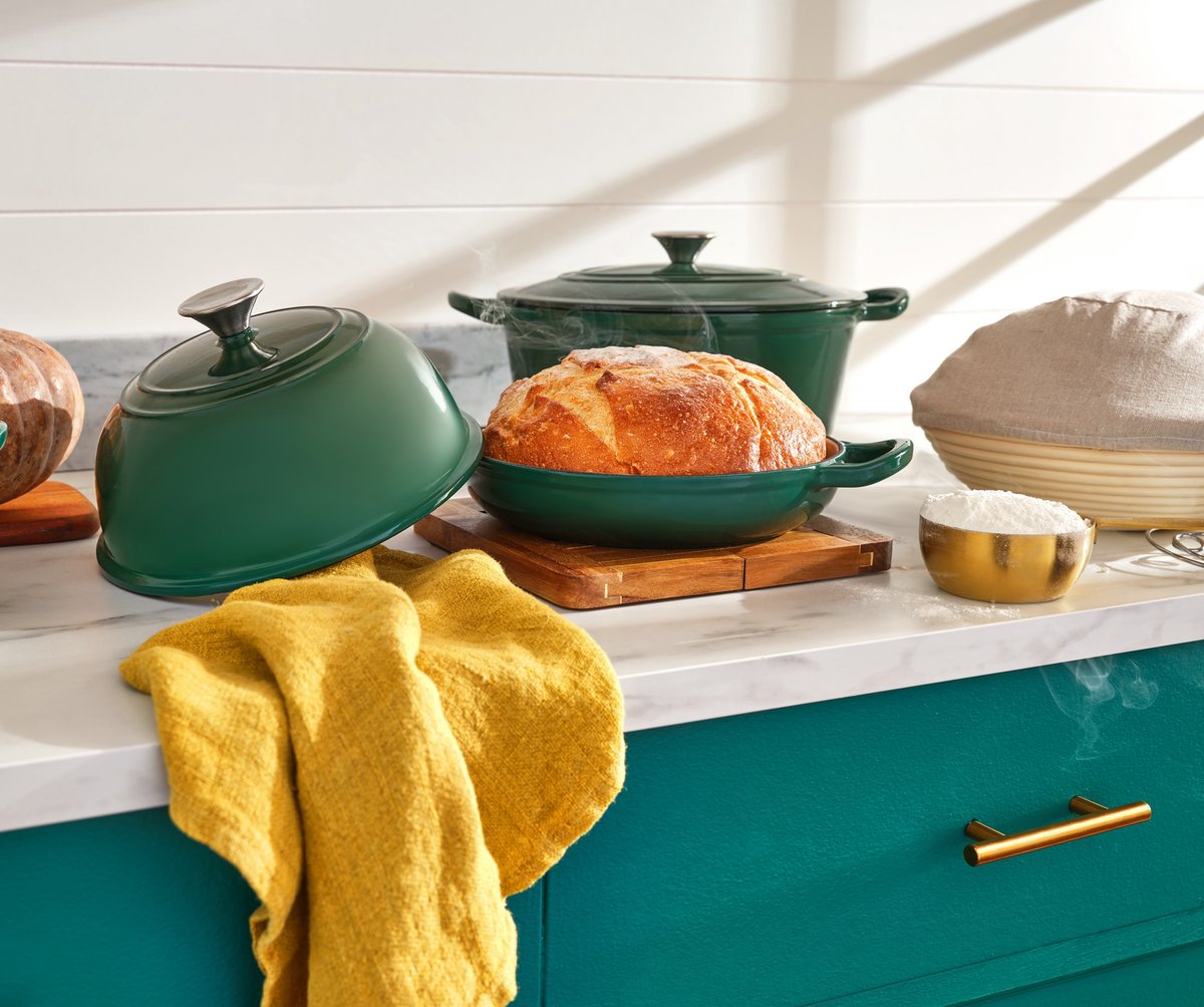 Green enamel casserole dishes and a fresh loaf on a teal kitchen island with a yellow cloth