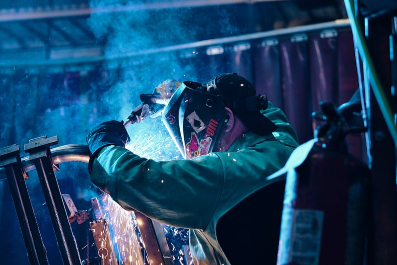 A welder in a dark workshop, sparks flaring from the torch in a haze of blue smoke