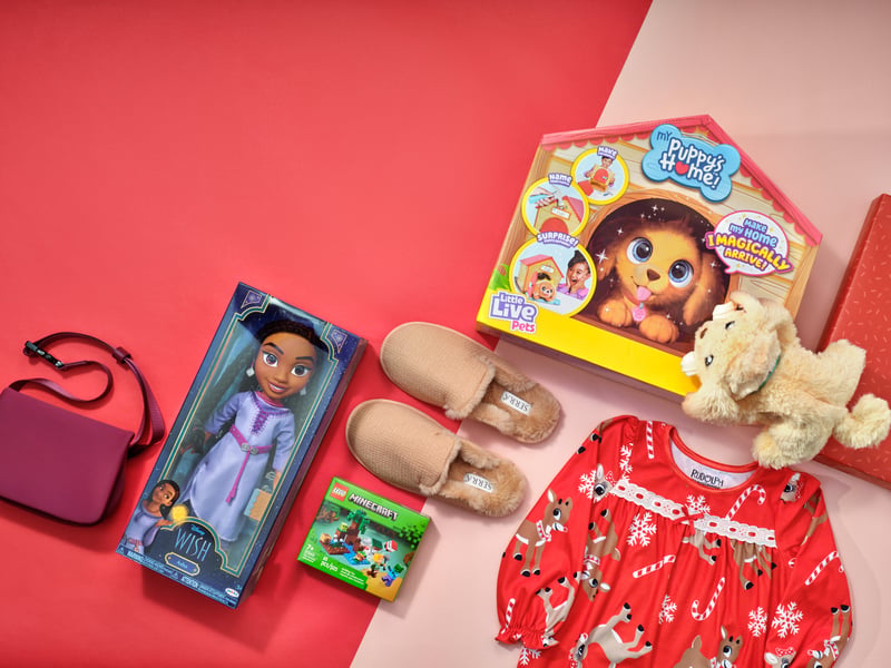 Children's gifts arranged on a pink and red ground — a doll, slippers, a red patterned nightdress and a plush toy