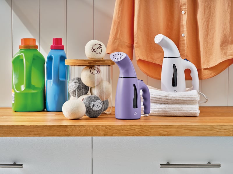 Laundry products, brushes and a garment steamer arranged on a wooden counter beneath a hanging shirt