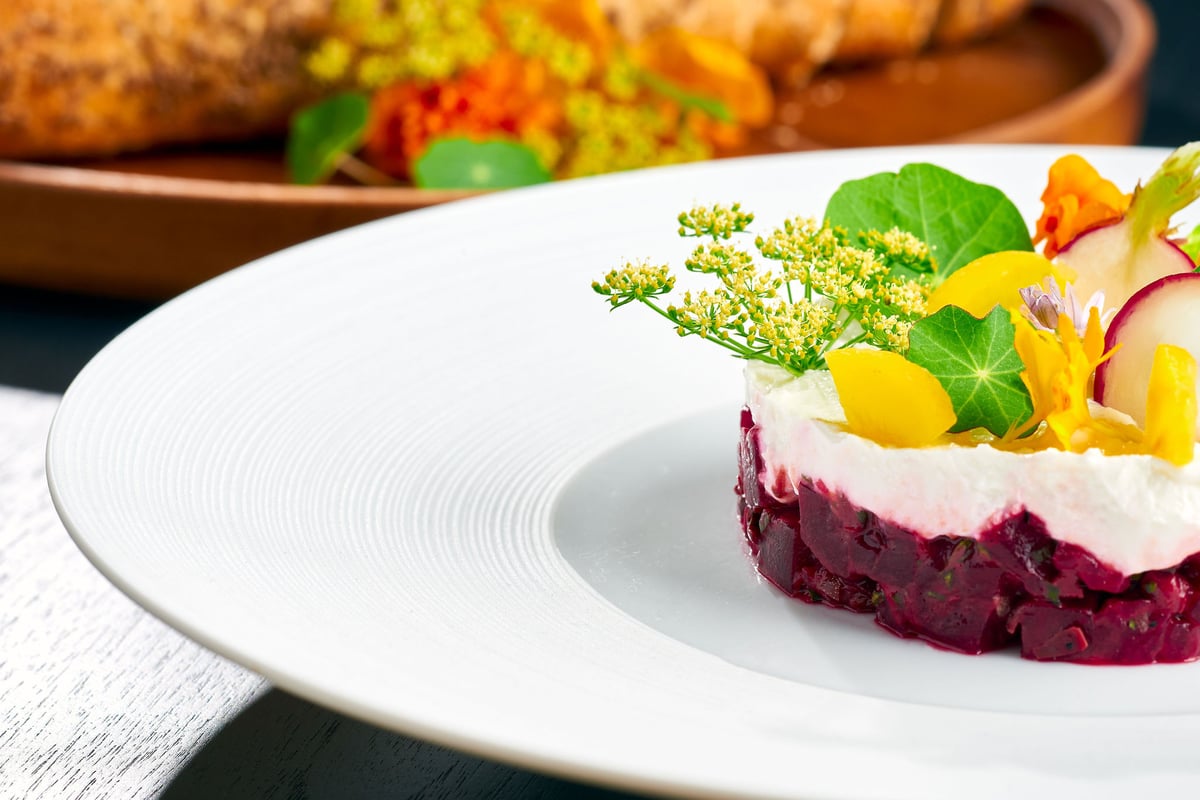 A plated beetroot dish topped with microgreens and edible flowers on a white plate