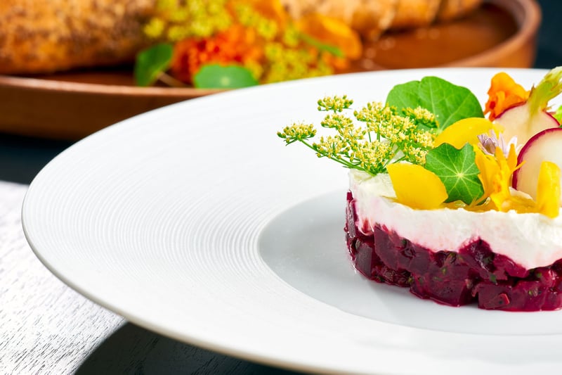 A plated beetroot dish topped with microgreens and edible flowers on a white plate