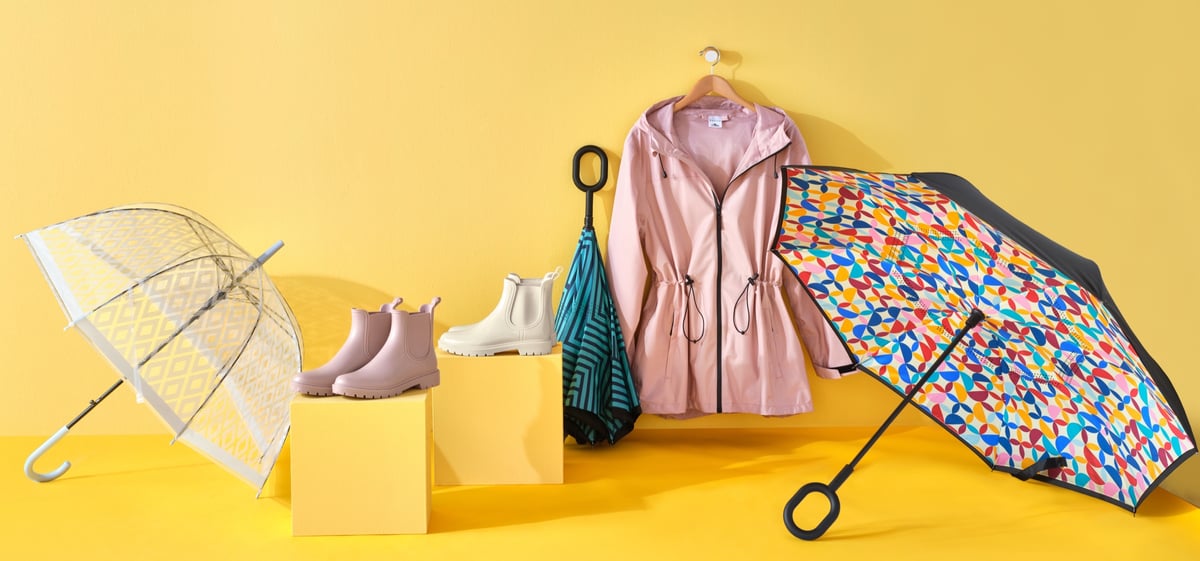 Umbrellas, rain boots and a dressing gown arranged as a group on a yellow ground