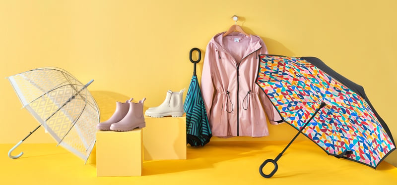Umbrellas, rain boots and a dressing gown arranged as a group on a yellow ground