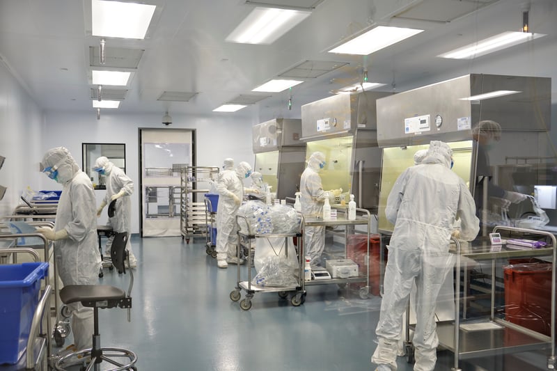 Technicians in full white cleanroom suits working along a stainless steel production line
