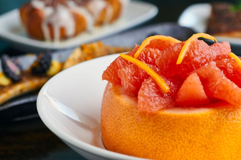 A hollowed grapefruit filled with citrus segments and peel, served on a white plate