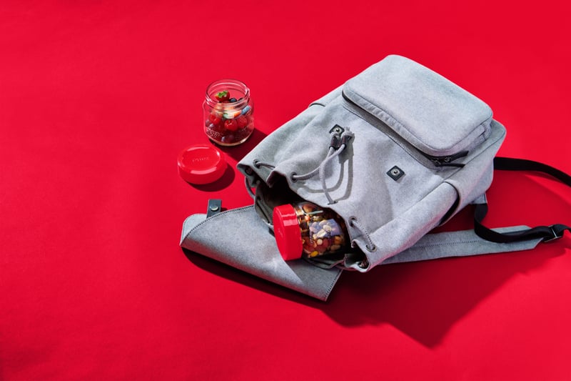 A striped backpack laid open on a red ground with lunch jars and a notepad spilling out