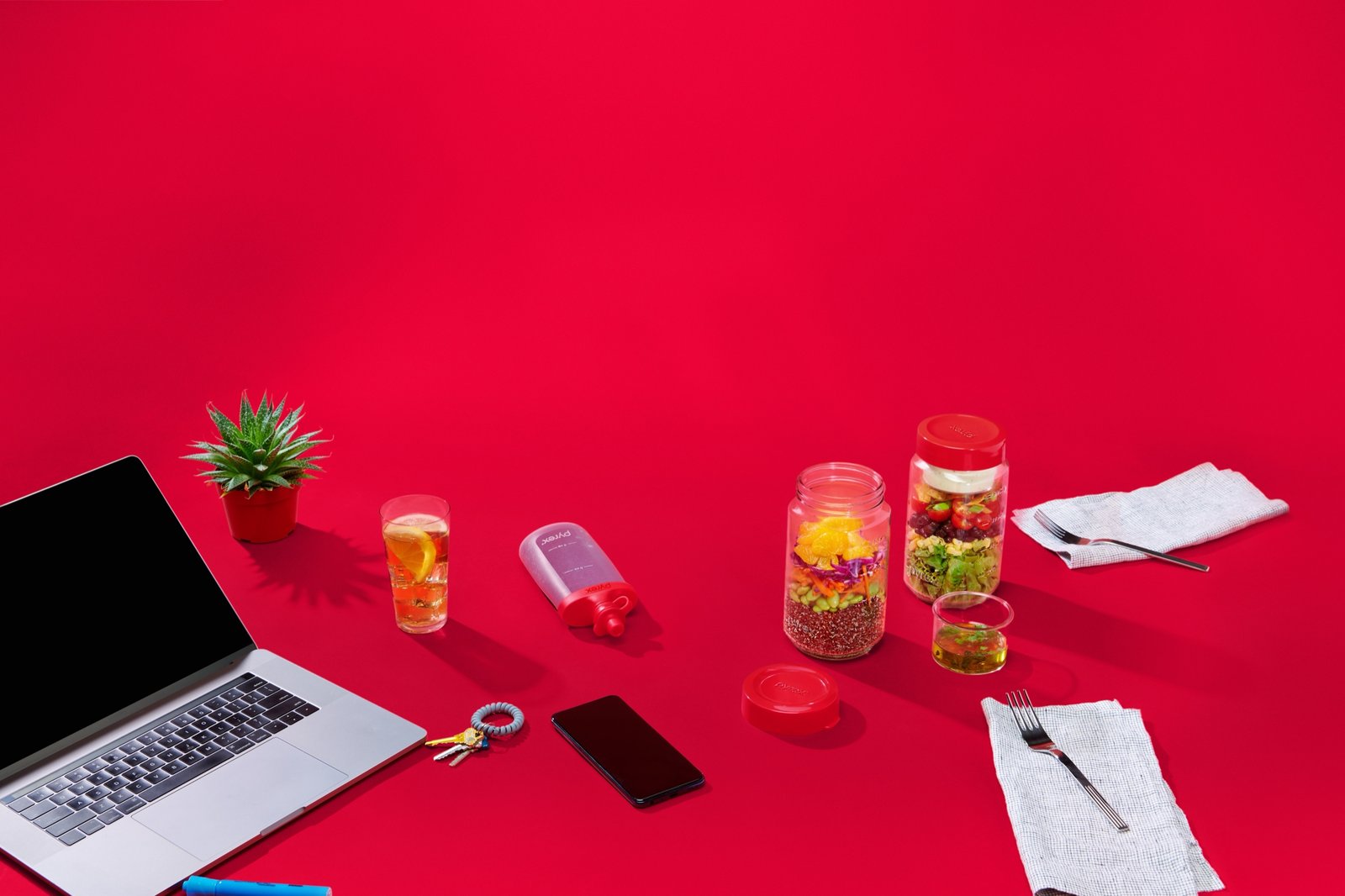 A laptop, phone and jars of sweets laid out on a saturated red desk surface