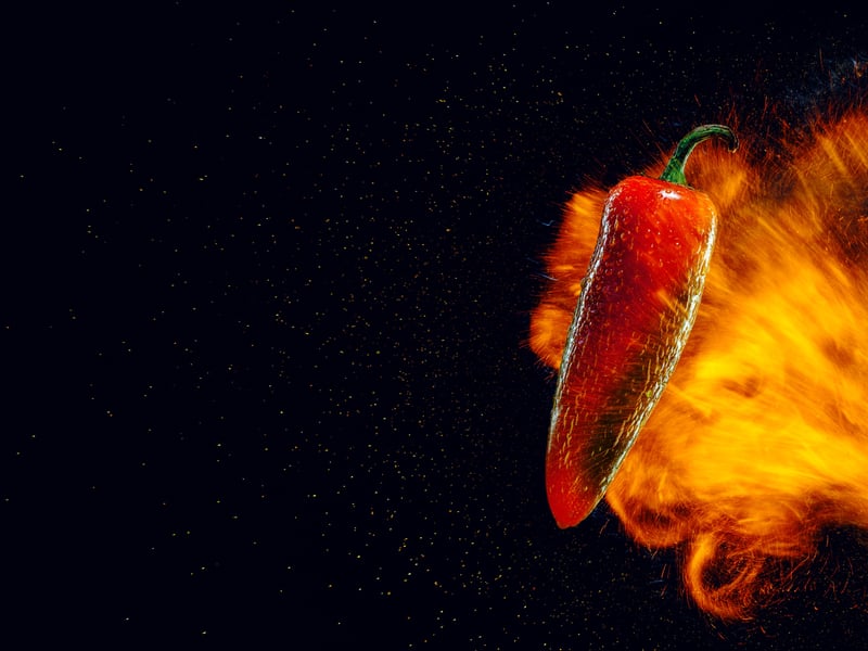 A red chilli photographed against black with a burst of flame behind it
