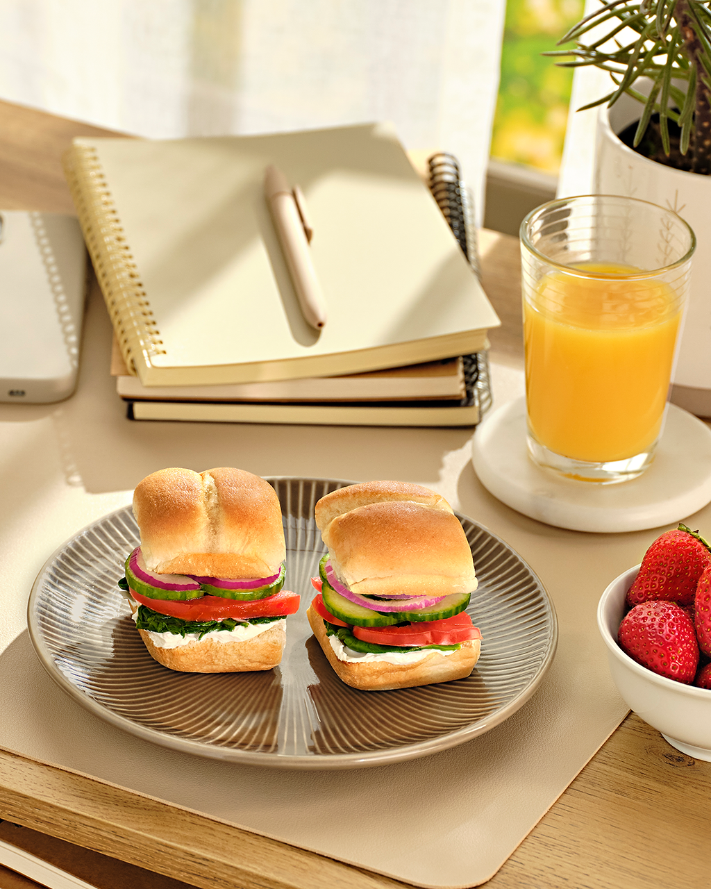 Two open sandwiches on a plate beside strawberries, orange juice and a notebook