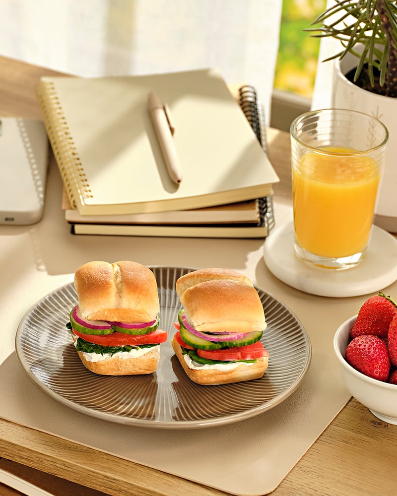 Two open sandwiches on a plate beside strawberries, orange juice and a notebook
