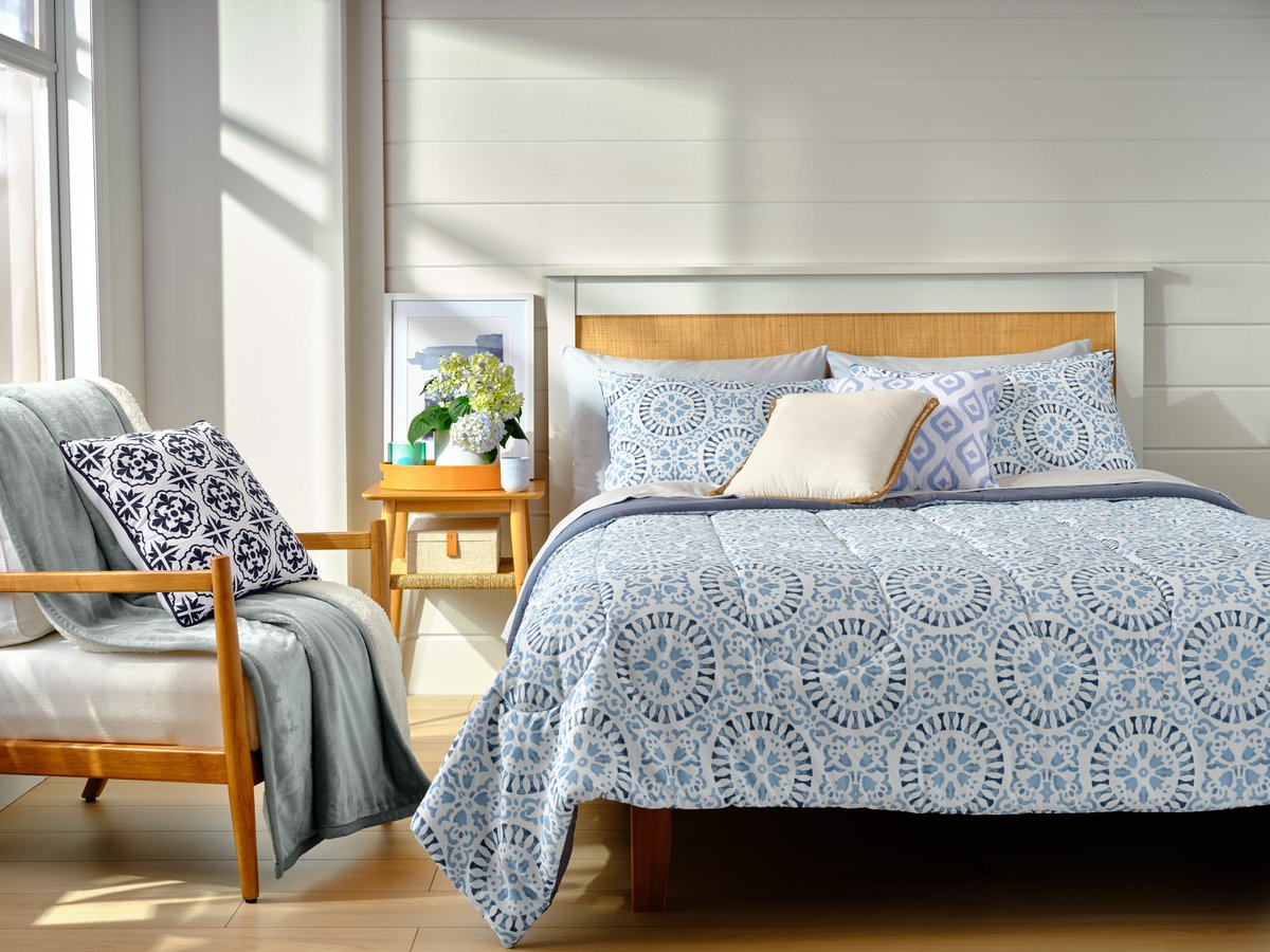 A bright bedroom with blue patterned bedding and a wooden bedside table in low sun