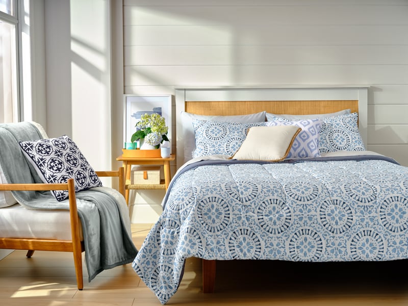 A bright bedroom with blue patterned bedding and a wooden bedside table in low sun