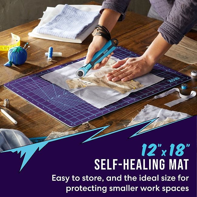Hands smoothing fabric on a purple cutting mat at a wooden work table