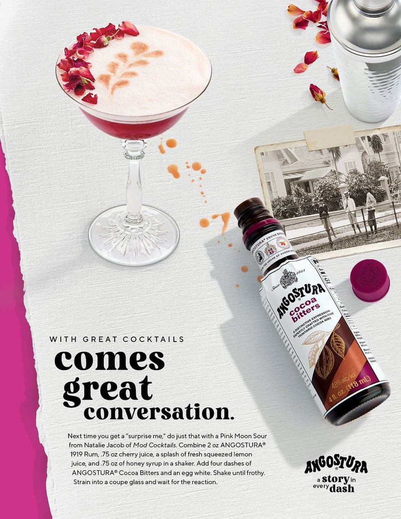 A foamed cocktail scattered with rose petals beside an Angostura bottle and a vintage photograph, laid out on textured paper