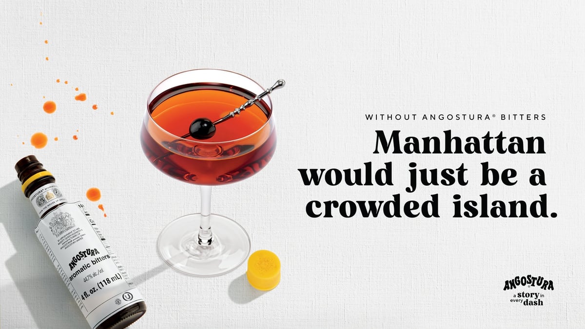 A Manhattan cocktail beside a bottle of Angostura bitters and a twist of lemon on textured paper