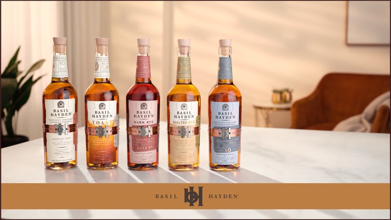 Five Basil Hayden bottles lined up across a marble counter in a softly lit room