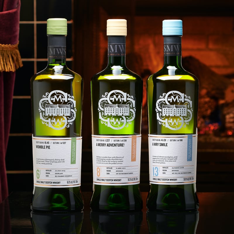 Three Scotch Malt Whisky Society bottles standing in a row in a warm, low-lit room