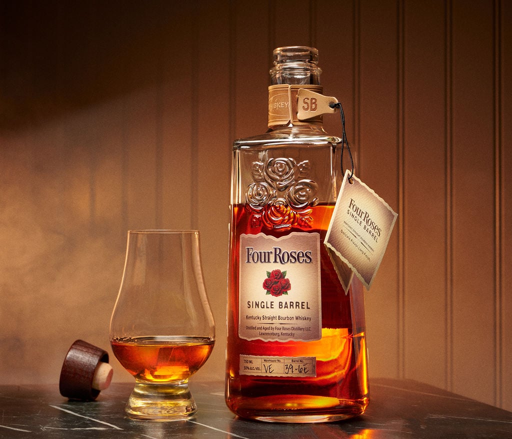 A bottle of Four Roses Single Barrel beside a Glencairn glass of bourbon on dark wood