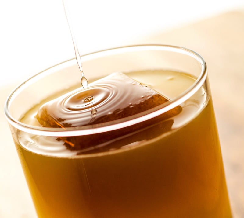 A droplet falls into a glass of amber liquid over ice, sending a ring of ripples across the surface