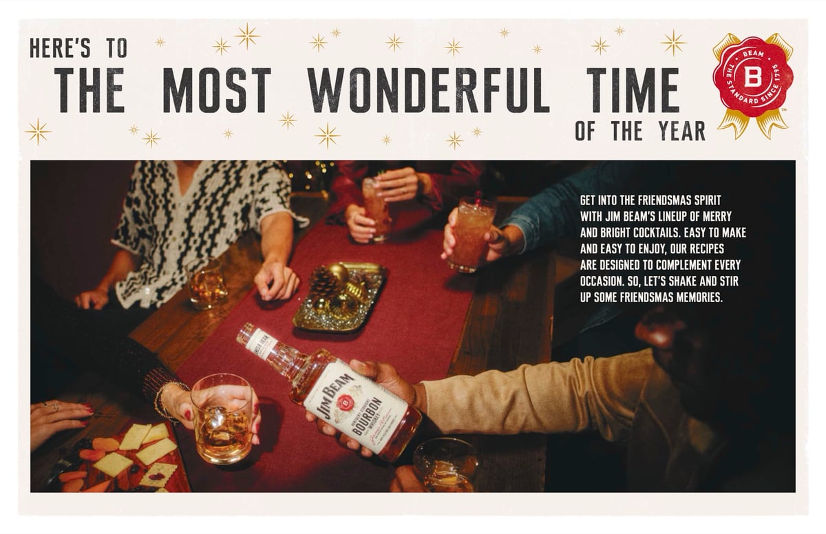 An overhead holiday scene of hands reaching across a red table set with bourbon glasses and snacks