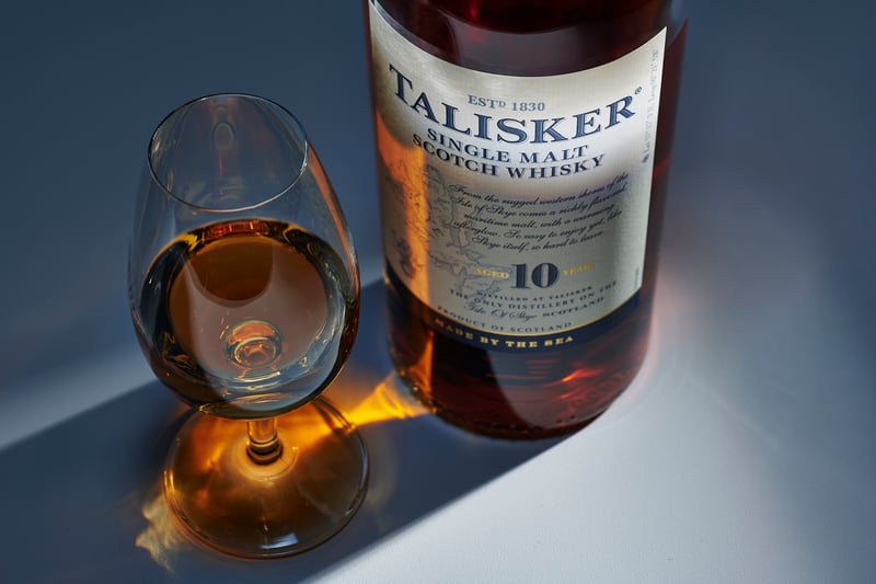 A Talisker 10 bottle beside a tilted nosing glass of whisky, lit cool against a pale ground