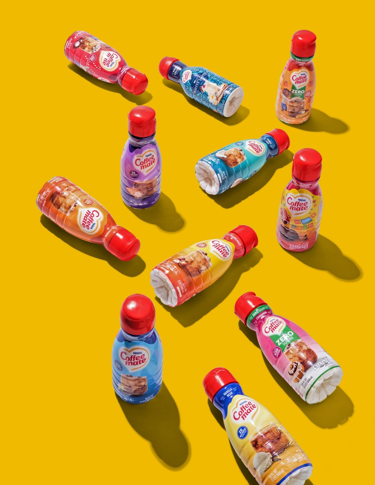Coffee Mate creamer bottles scattered across a saturated yellow ground, casting hard shadows