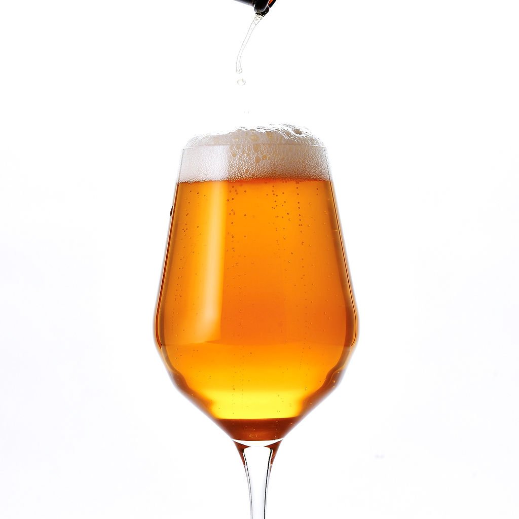 A stemmed glass of amber beer with a thick head, photographed against white