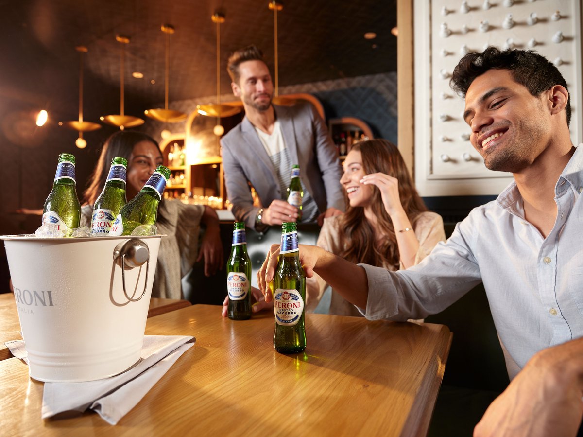 Friends talking around a bar table with bottles of lager and an ice bucket in the foreground