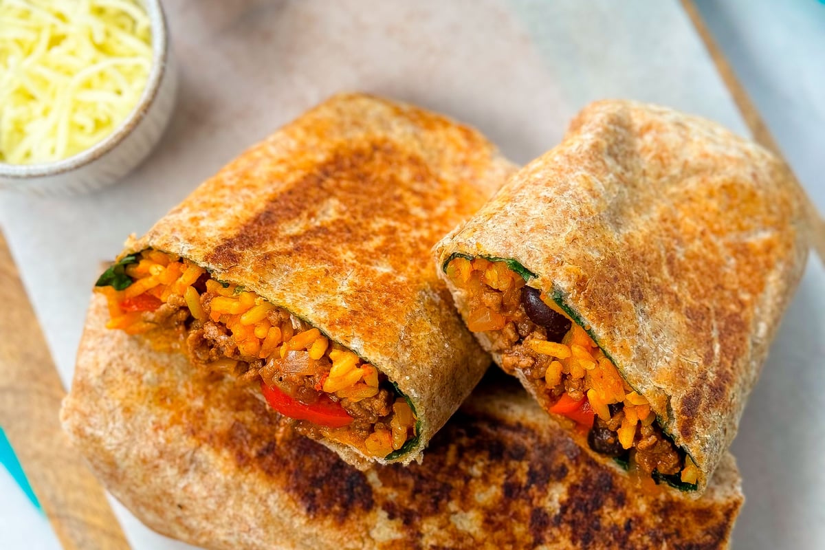 Grilled burrito cut in half showing rice, beans, and vegetables with salad and cheese bowl