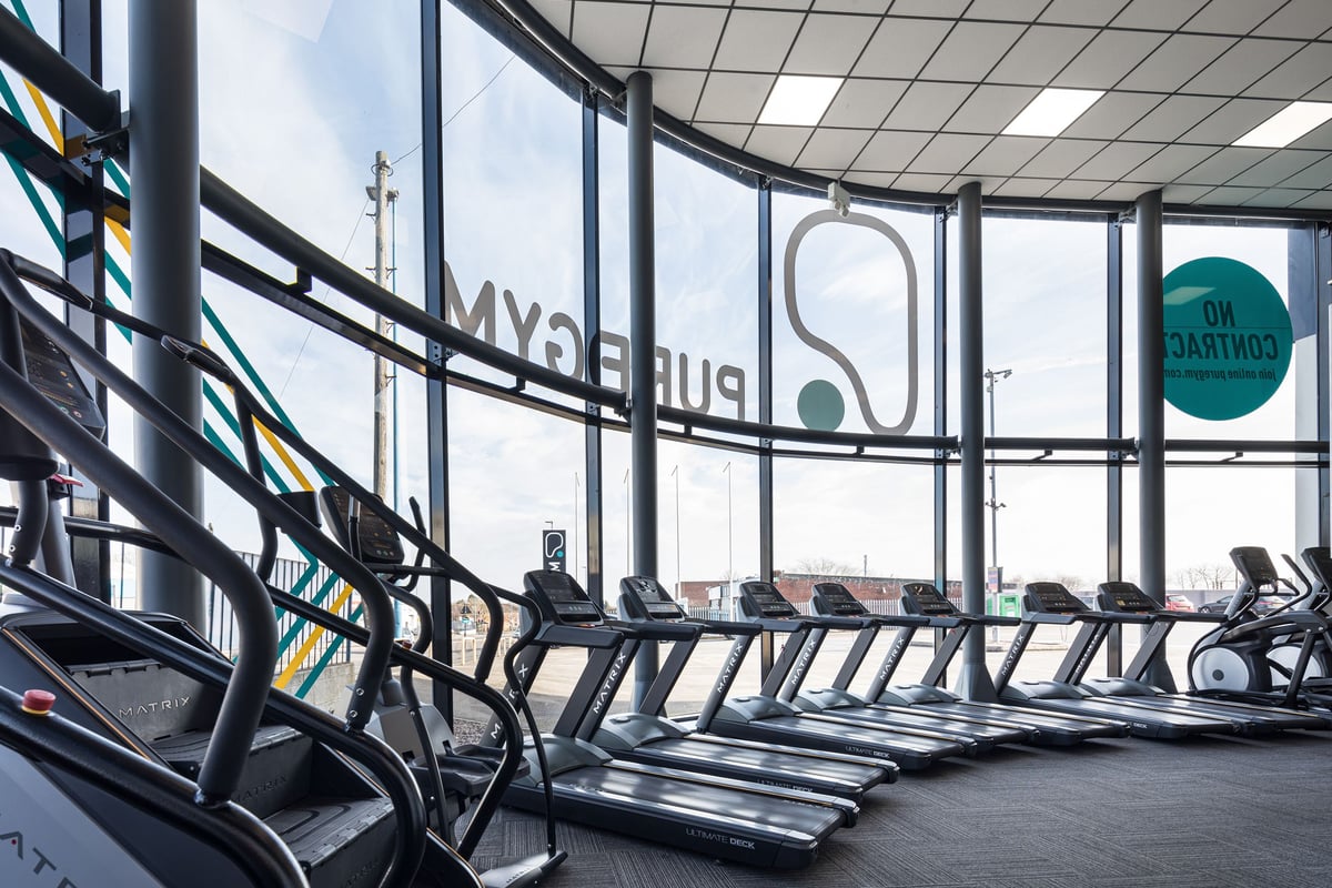 PureGym Dudley Tipton: Rows of treadmills and elliptical trainers inside a bright gym area with floor-to-ceiling windows.