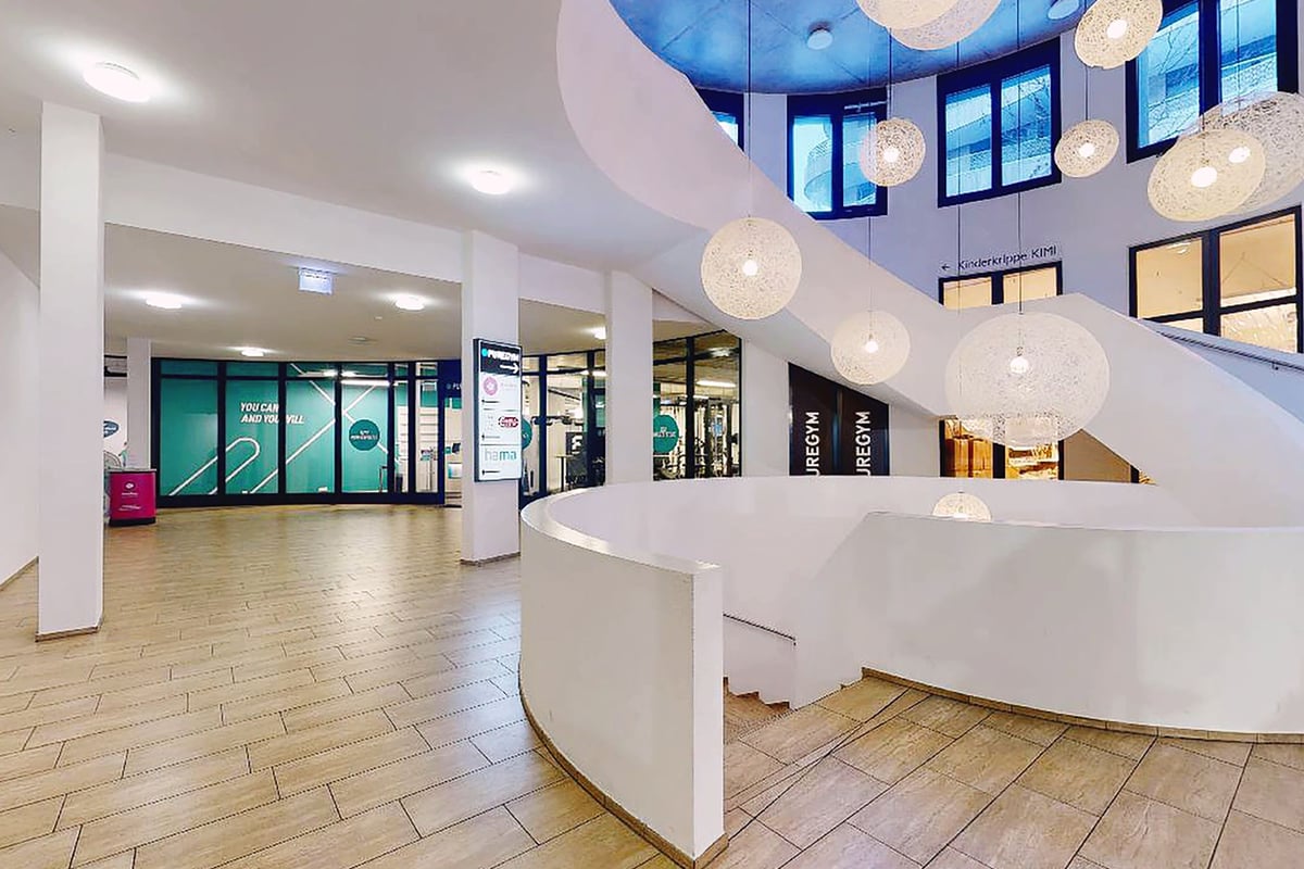 PureGym Chur: Innenlobby im Fitnessstudio mit Kugelbeleuchtung, Rezeption, Digitalanzeigen und modernem Sitzbereich.